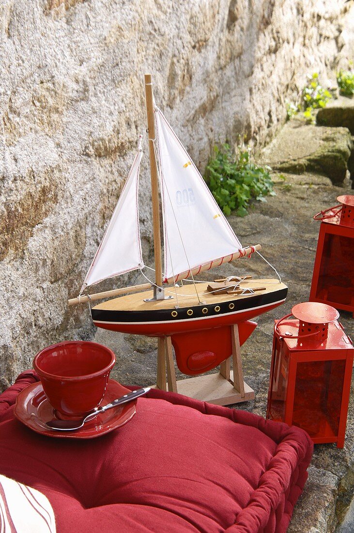 Steinbank auf Terrasse mit Sitzkissen, Laterne und Modell-Segelboot in Rot