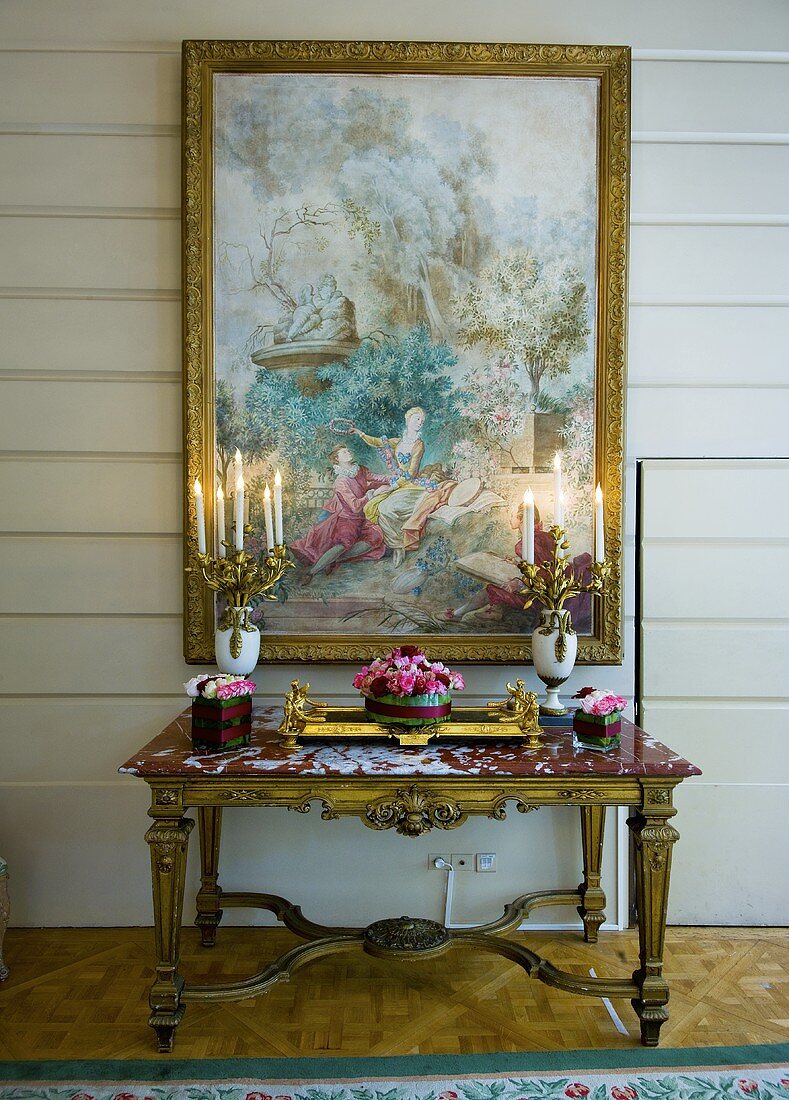 Antiker Wandtisch mit Kerzenleuchtern, Blumenschmuck und darüber hängendem Wandgemälde