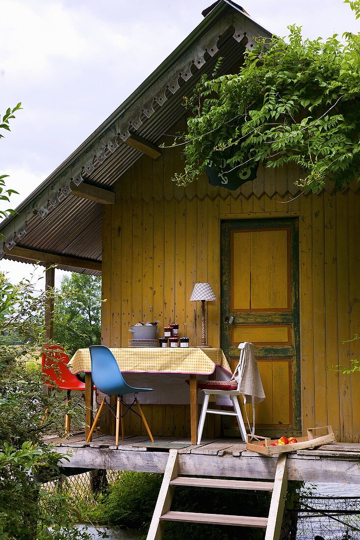 Tisch und Stühle auf Terrasse vor kleinem Holzhäuschen