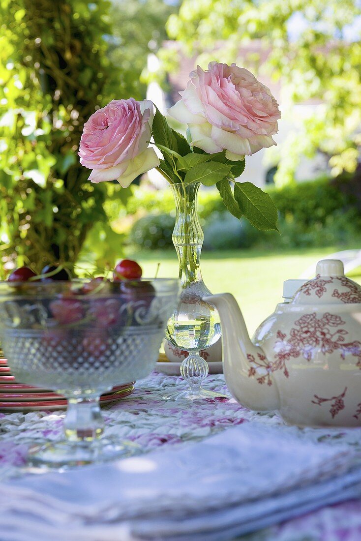 Teekanne, Kirschen und Rosen auf Gartentisch (Schlossgarten La Verrerie, Frankreich)