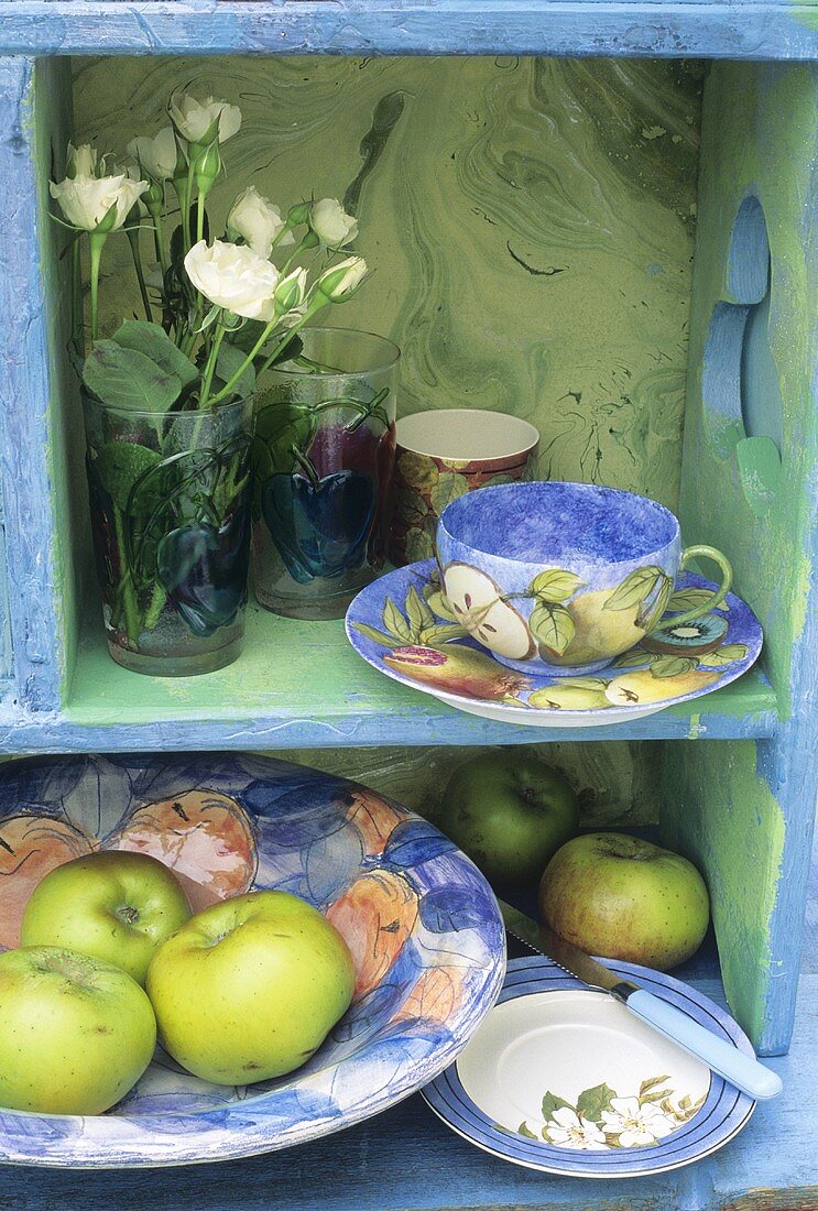 Regal mit Kaffeetasse, Blumen & Äpfeln in einer Schale