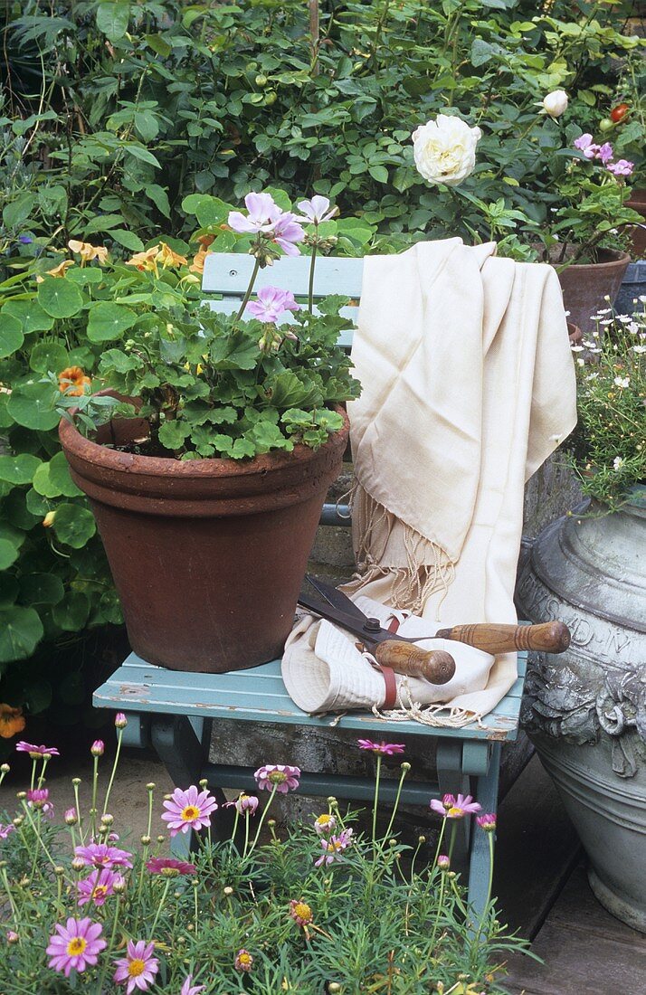 Gartenszene: Topf mit Geranien & Gartenschere auf Klappstuhl