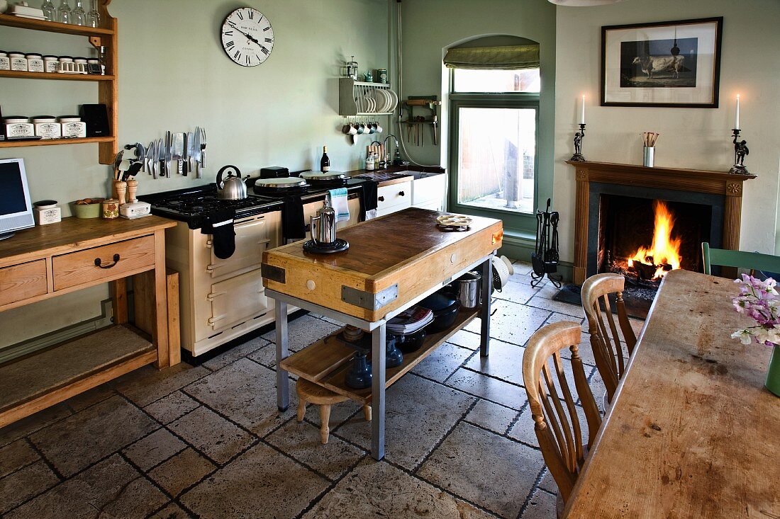 Ländliche Küche mit Steinboden, Hackstock, Esstisch und Kaminfeuer