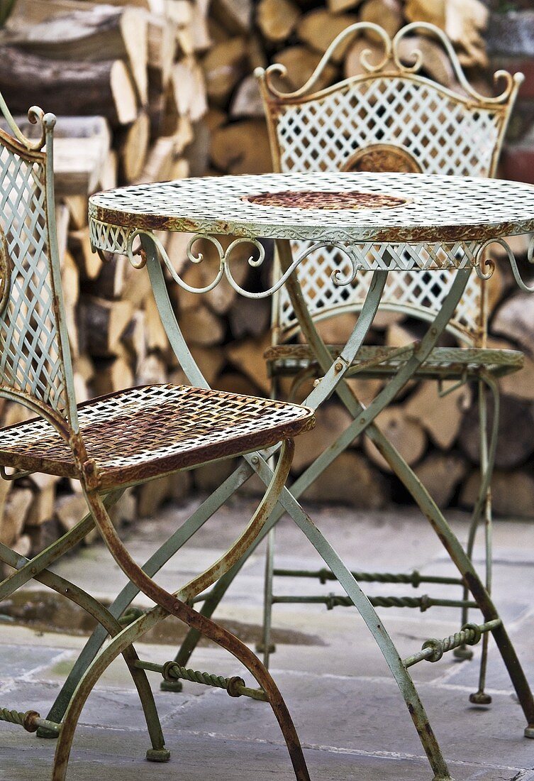 Old iron chairs and small table in front of a woodpile