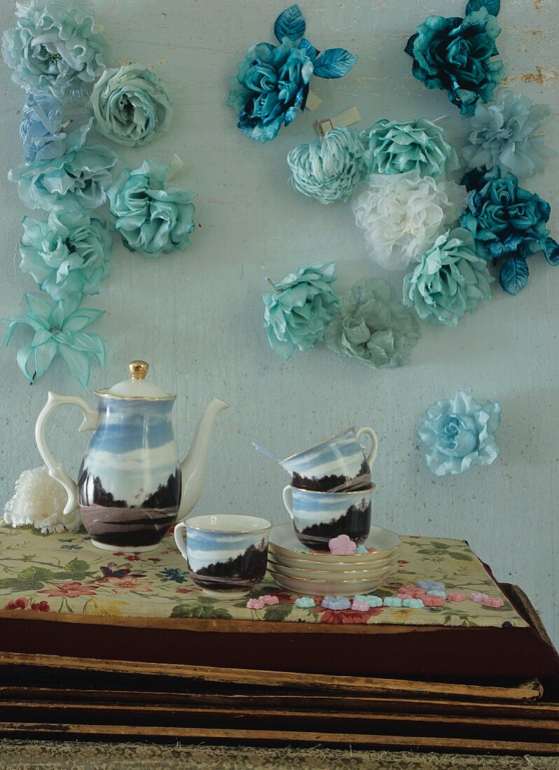 Painted coffee service in front of turquoise wall with fabric flowers