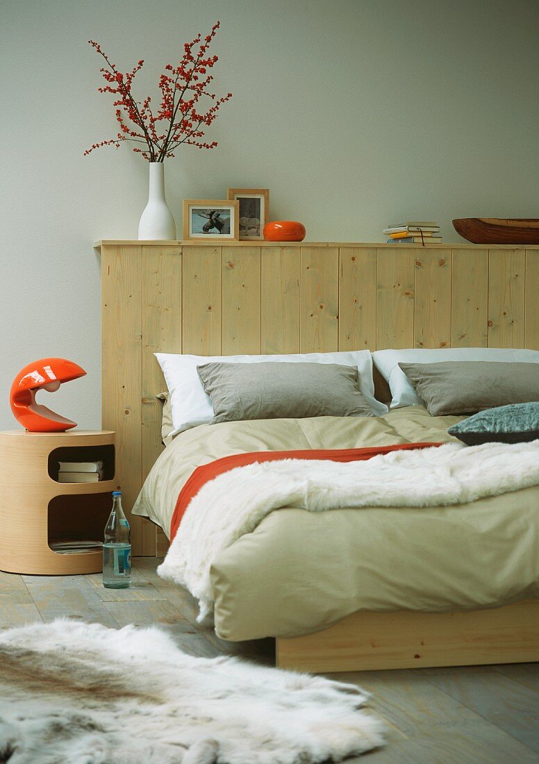 Doppelbett mit Kopfende aus Holz, Nachttischchen mit Lampe & Tierfell als Bettvorleger