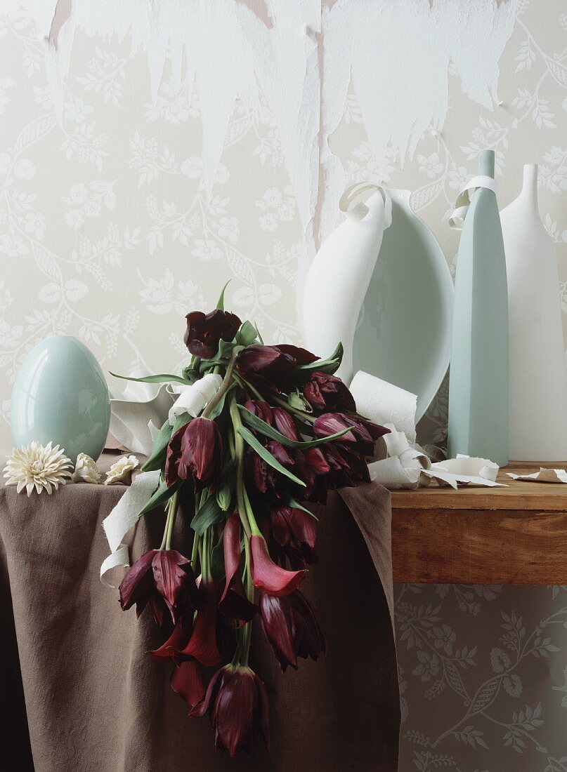 Vases and a bouquet of purple zantedeschia and tulips in front of torn wallpaper