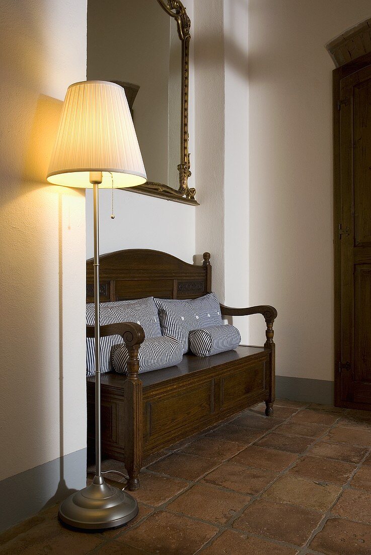 Stehlampe mit Stoffschirm und antike Sitzbank auf Terrakottaboden