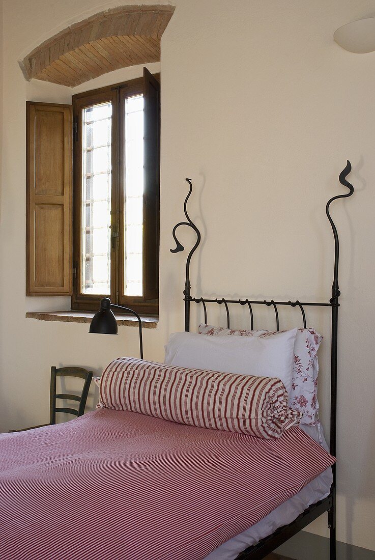 Schmiedeeisernes Bett mit rosa Bettwäsche und Nackenrolle neben Fenster