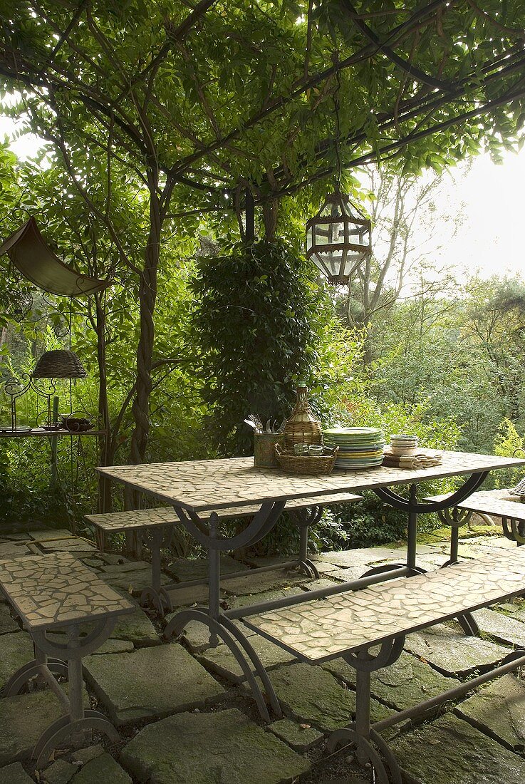 Table and benches under a pergola covered in greenery