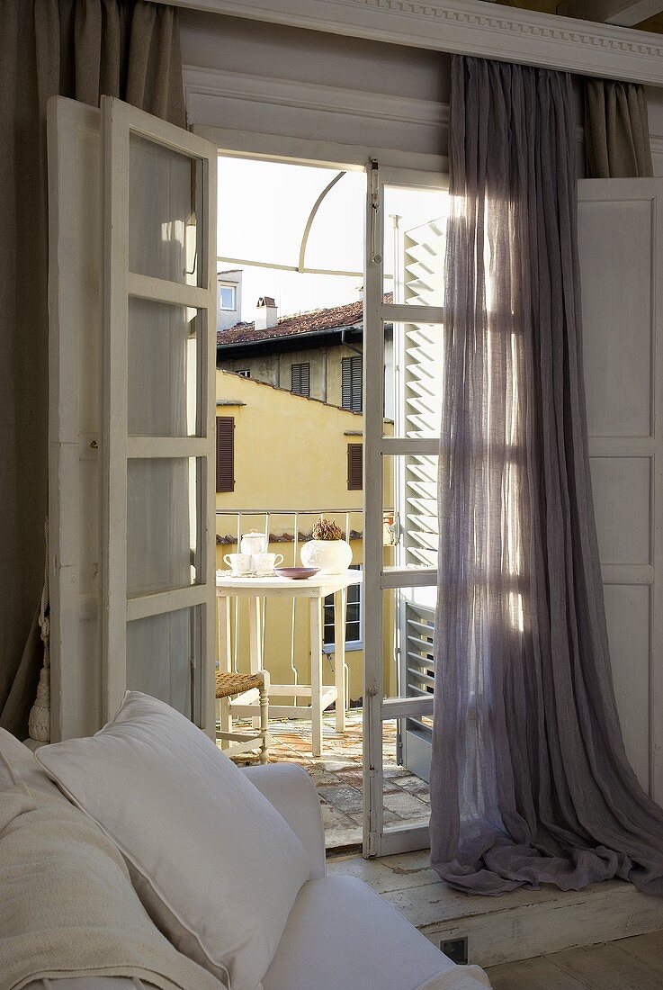 Offenstehende Balkontür mit bodenlangem Vorhang und Blick auf Frühstück im Freien