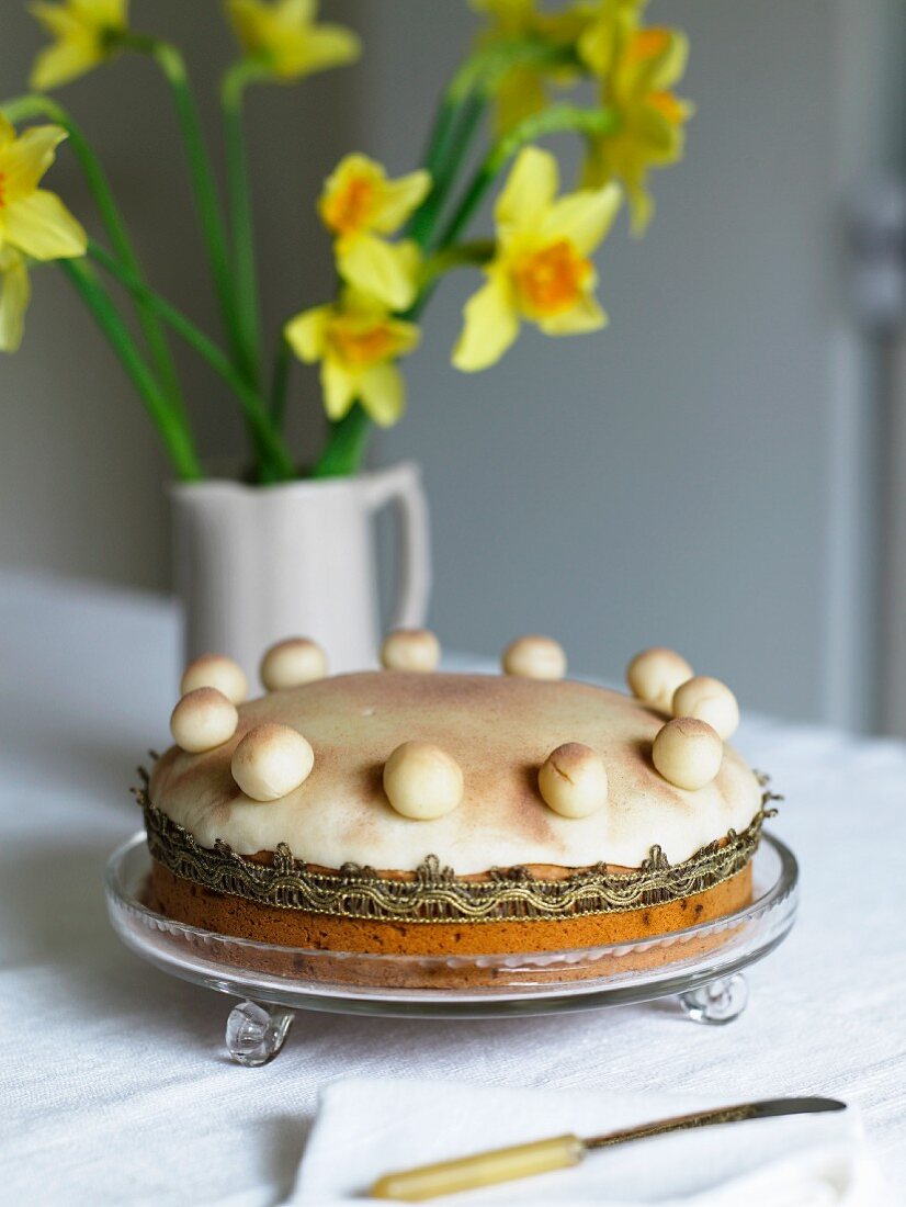 A cake in a shallow glass bowl and a vase of daffodils