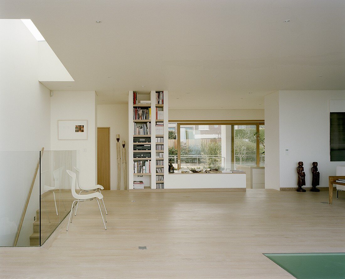 Offener moderner Wohnraum mit Parkettboden und Stühlen vor Glasbrüstung des Treppenaufgangs und Einbauregal