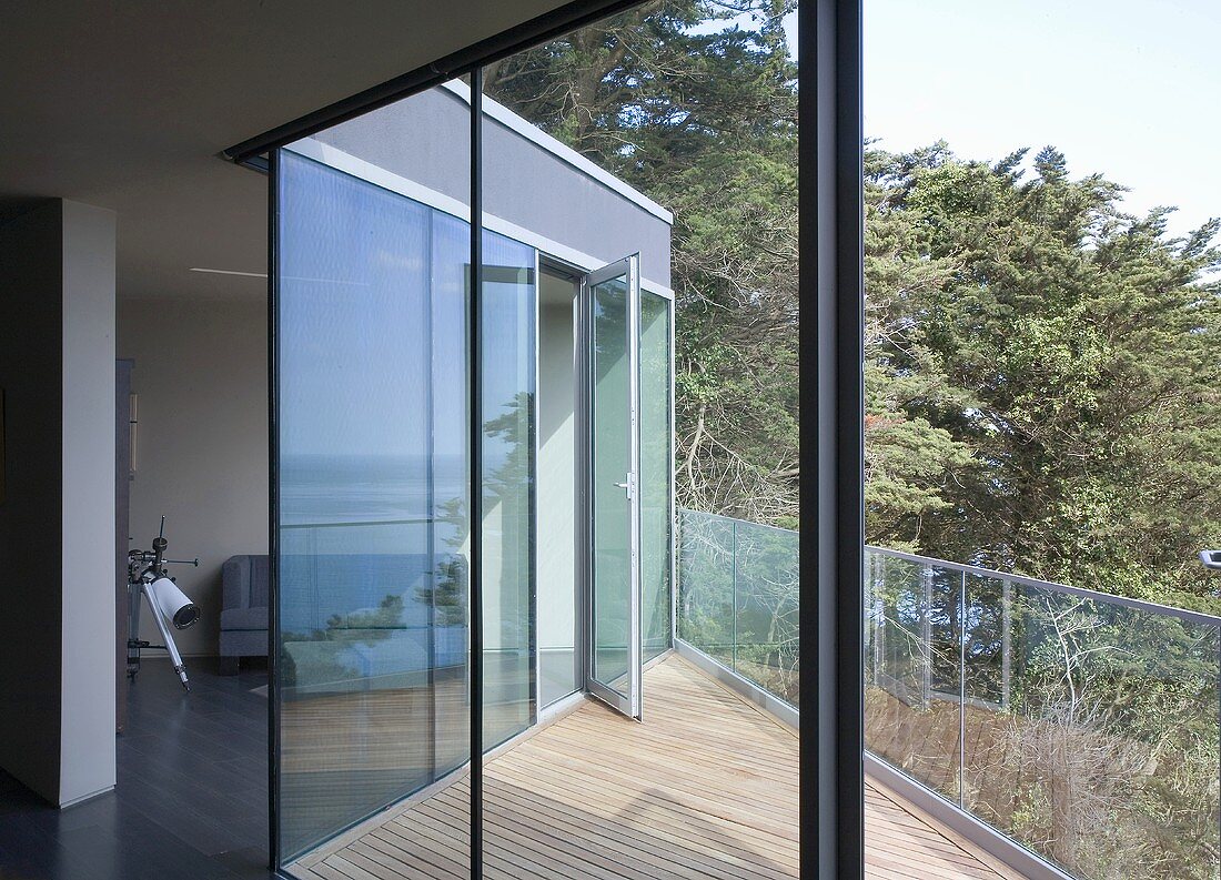 Blick durch offene Terrassentür auf Terrasse mit Holzdielen und Glasbrüstung eines modernen Wohnhauses