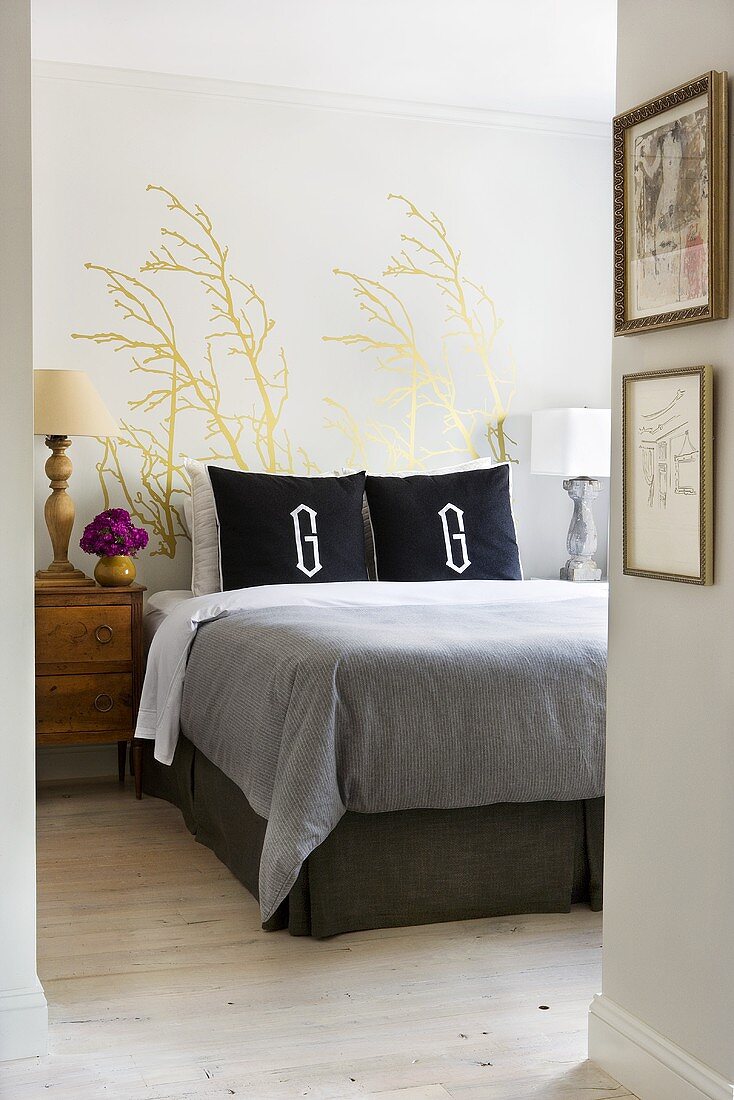 Blick in ein helles, stilgemixtes Schlafzimmer mit großem Doppelbett und antikem Nachttisch vor goldener Wandmalerei