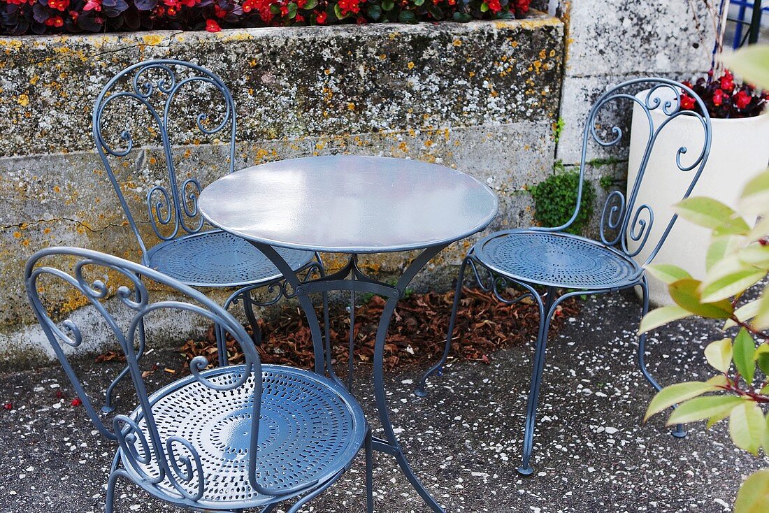 Gartentisch und Metallstühle auf herbstlicher Terrasse (Frankreich)