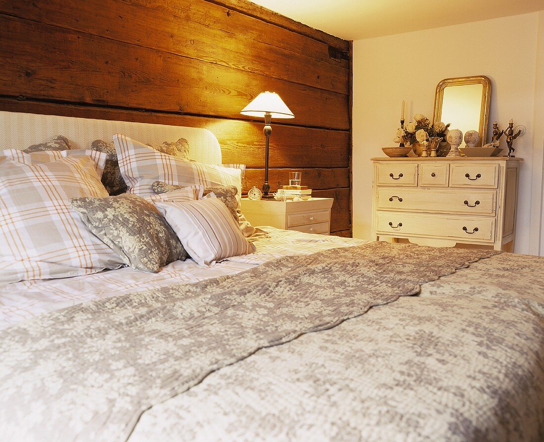 Großes Doppelbett mit gepolstertem Kopfende vor rustikaler Holzwand
