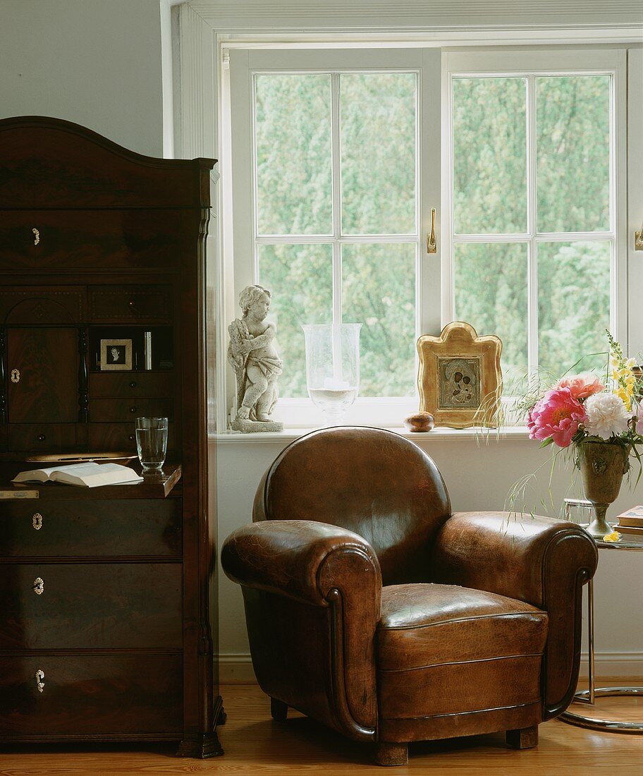 Antiker Ledersessel unter dem Fenster; daneben ein dunkelbrauner Sekretär mit aufgeklappter Schreibfläche
