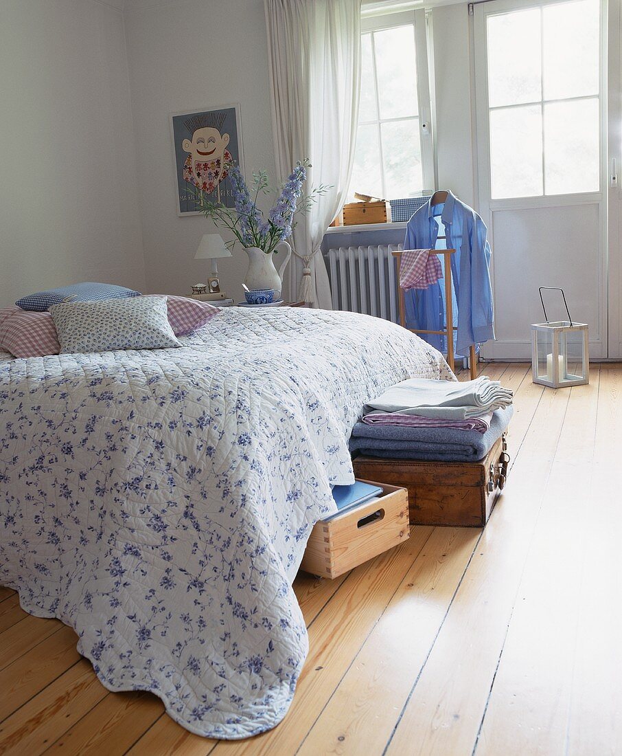 Grosses Doppelbett mit geblühmter Steppdecke in Schlafzimmer mit hellem Holzdielenboden