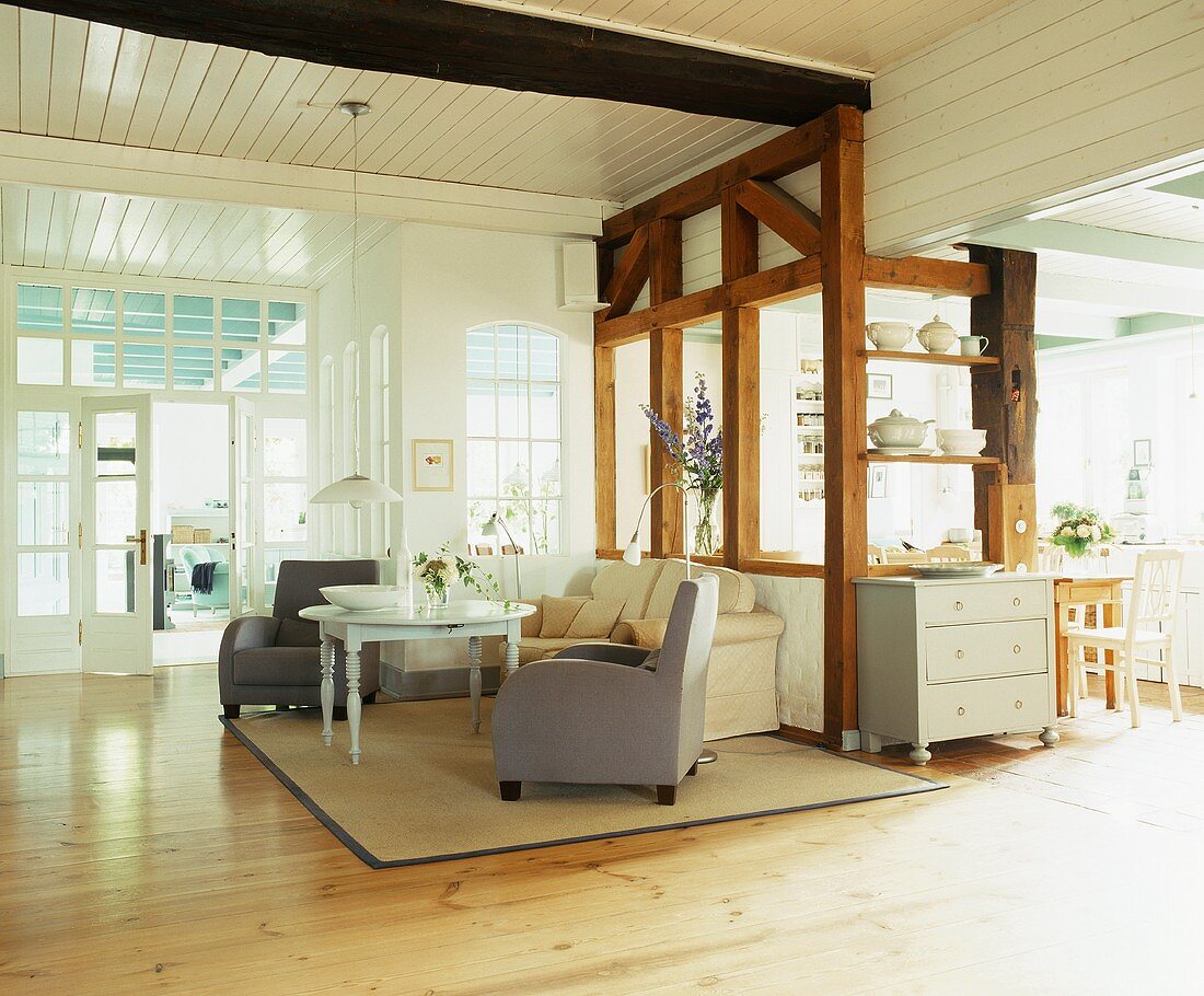 Weitläufiger, offener Wohnraum mit Wohnzimmer im Stilmix, einem rustikalen Holzgerüst und dahinter angrenzendem Küchenbereich