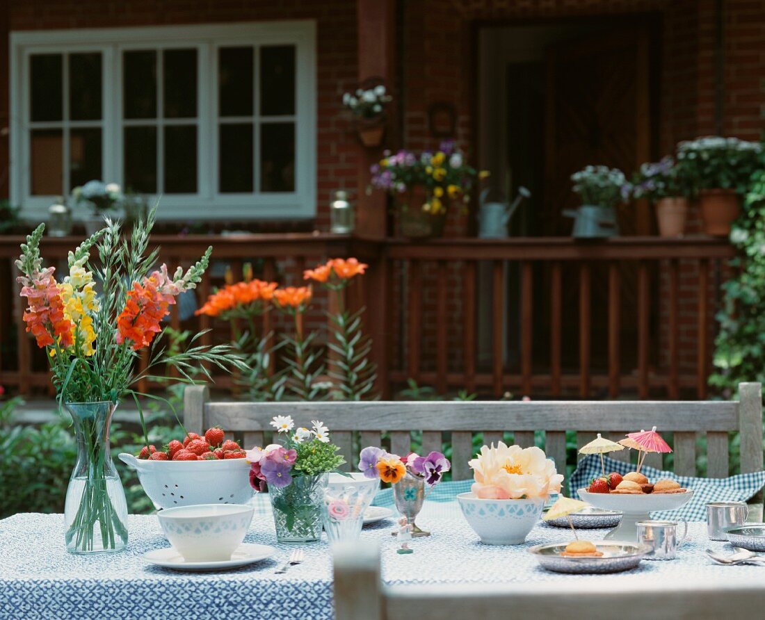 Tisch mit Blumen, Erdbeeren, Gebäck und Tassen im Freien
