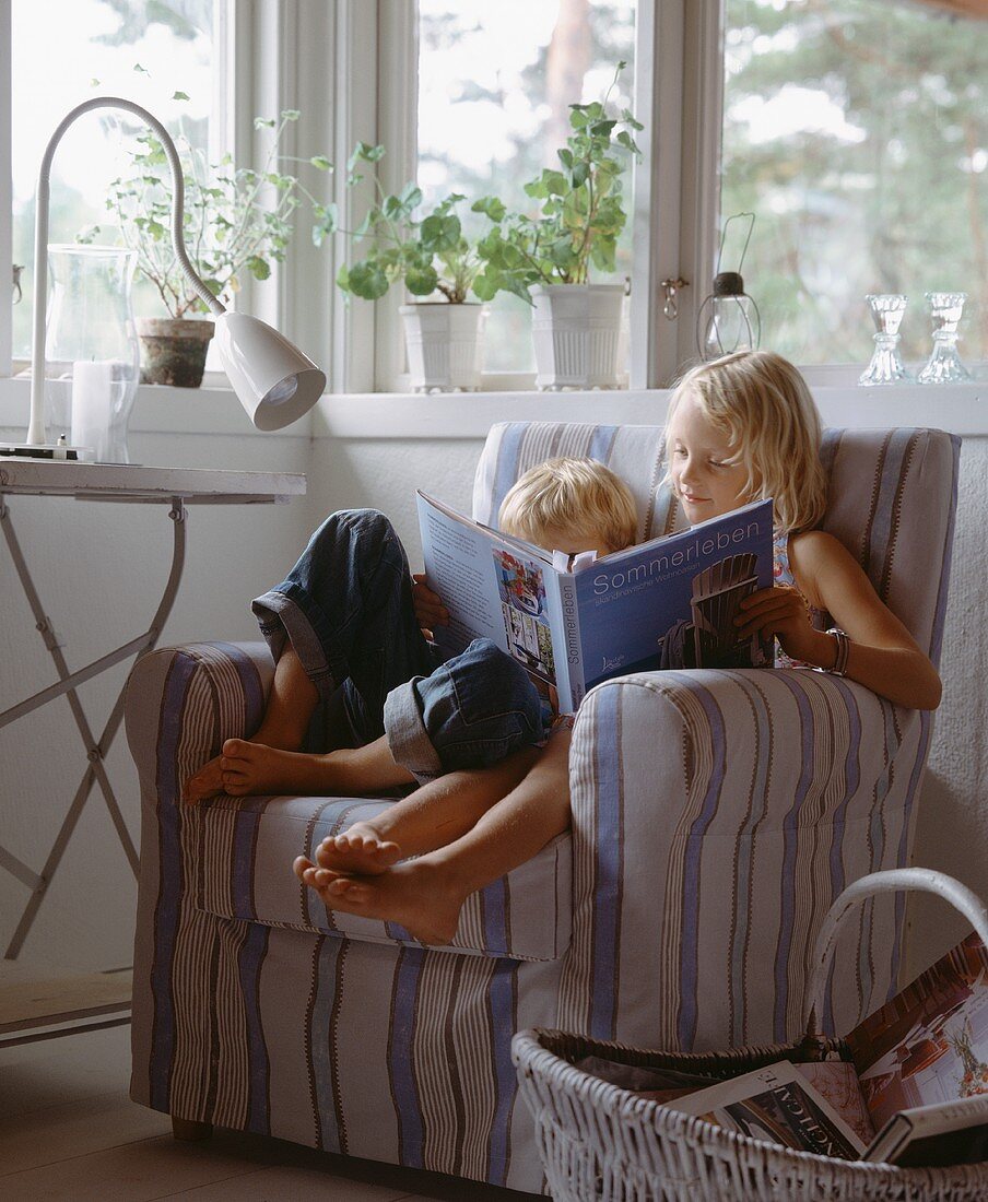 In einem gestreiften Sessel sitzende Geschwister, ein Buch lesend