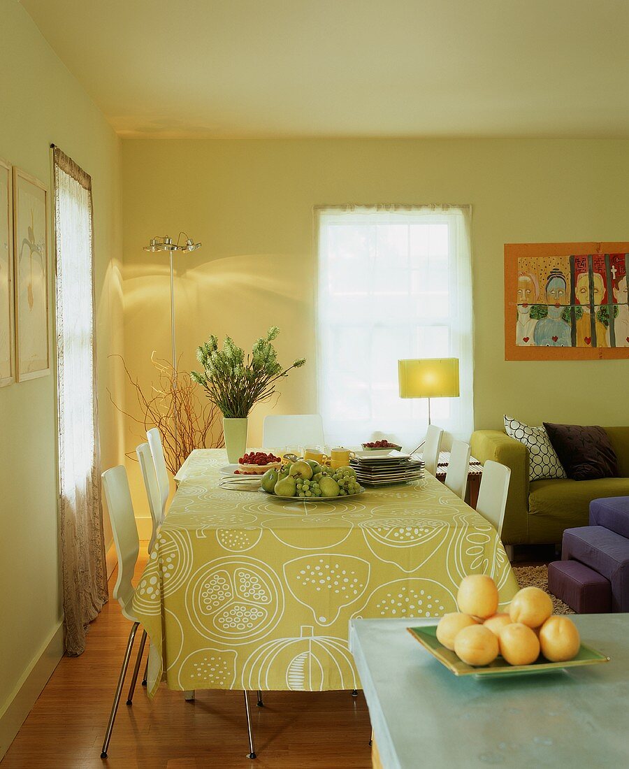 Freundliche Esszimmerecke mit fröhlicher Tischdecke mit Zitrusmotiven, Obstschale und Blumenstrauss
