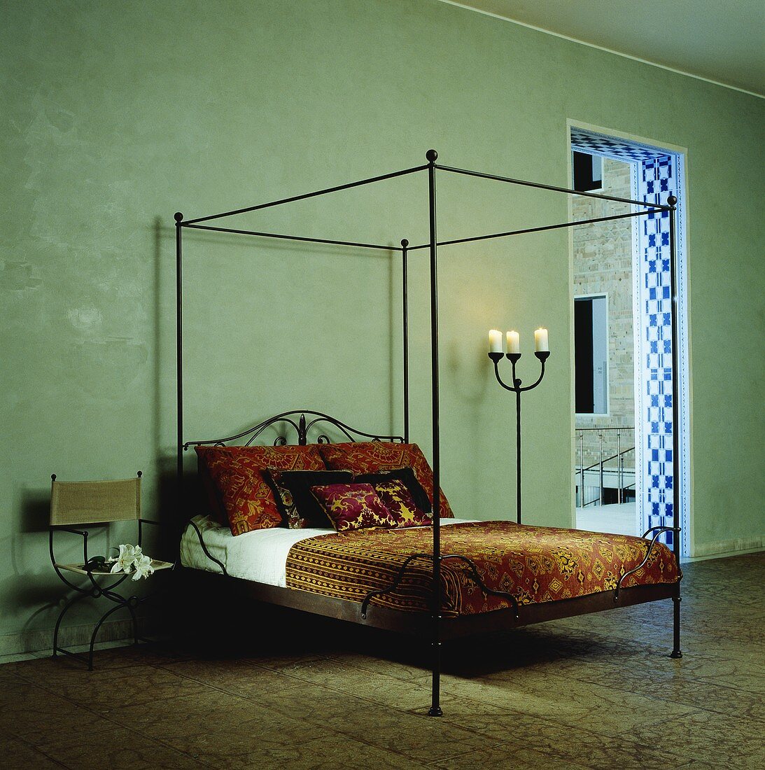 A green room with a black, steel-framed four-poster bed and oriental bed clothes