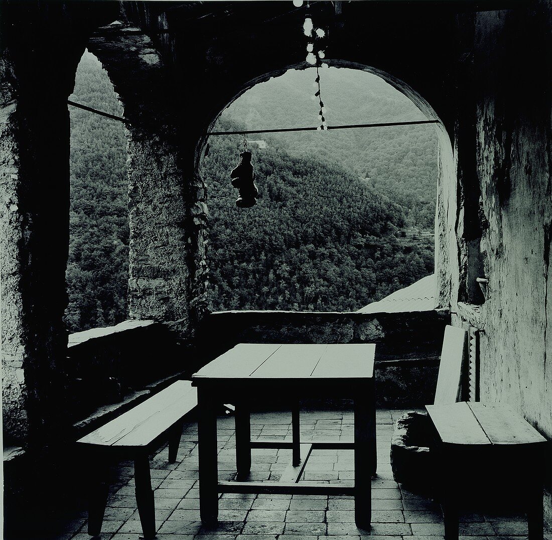 Alte Terrasse mit Rundbögen aus Stein und einer Holztischgarnitur (Schwarz-Weiß-Aufnahme)