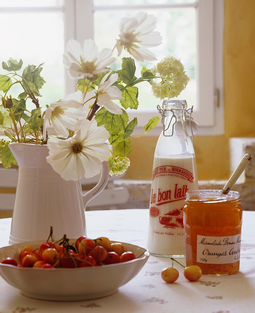 weiße Blumen, Schale mit Kirschen und Orangenmarmelade auf dem Tisch