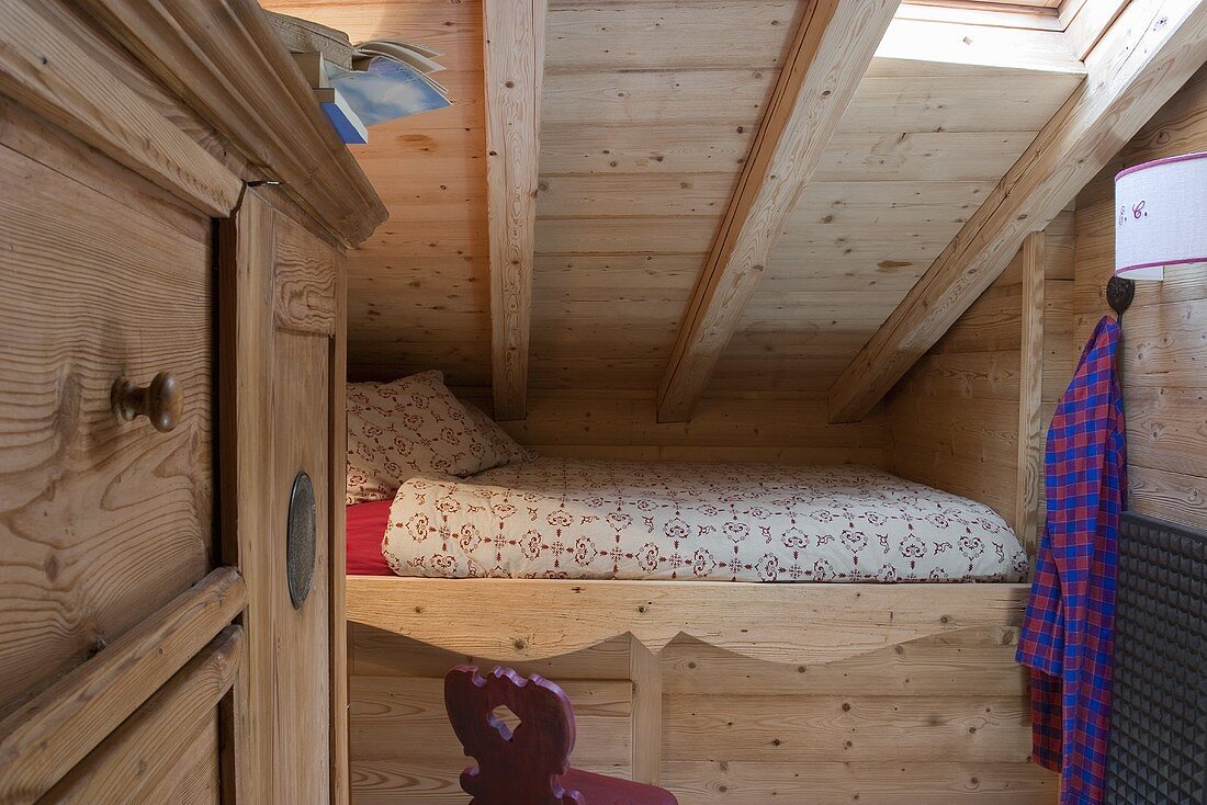 A built-in bed under the roof of a wood panelled room