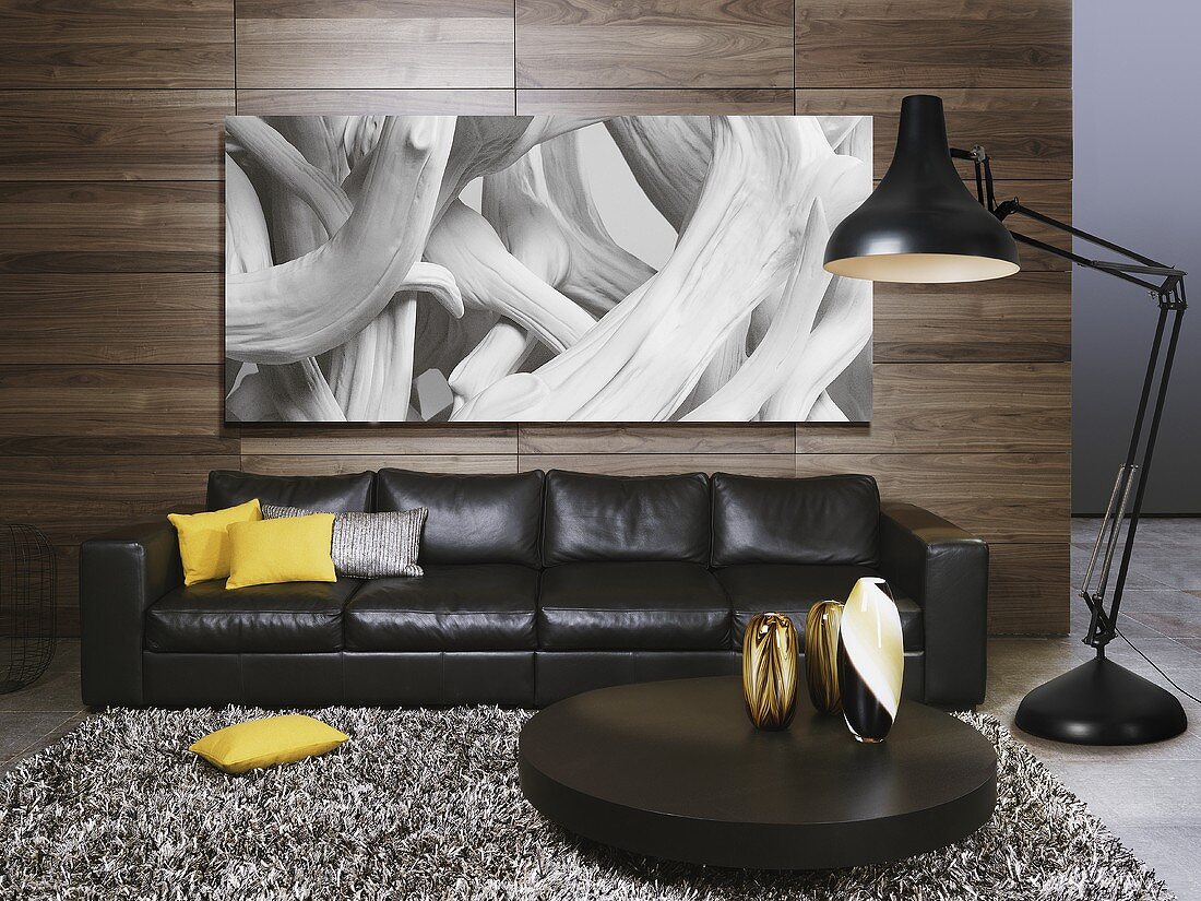 A black leather sofa and a coffee table with a floor lamp in front of a wood panelled partition wall with a photo hung on it