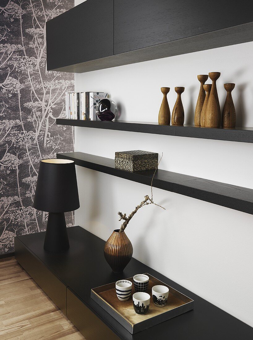 Wohnraumecke mit Tischleuchte & Deko-Objekten auf schwarzem Schrankboard & schwarzen Wandregalbrettern