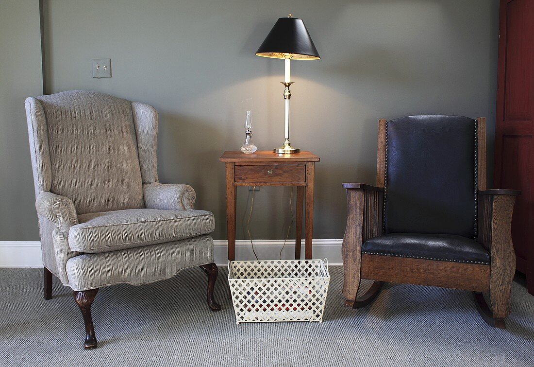 Sitzecke mit grauem Polstersessel, antikem Ledersessel & Beistelltischchen aus Holz mit Tischleuchte