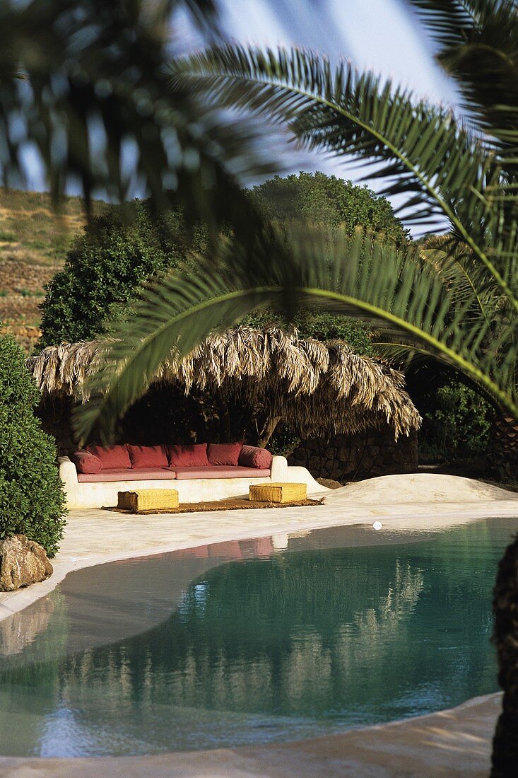 Pool unter Palmen und eine Couch im Innenhof eines Dammuso (Pantelleria, Sizilien, Italien)
