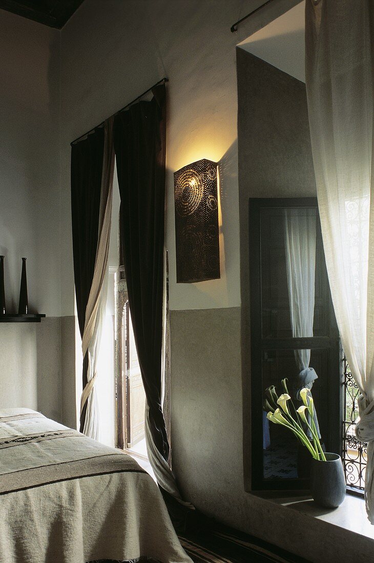 Marokkanisches Schlafzimmer mit Bett, bodenlangen Fenstervorhängen & orientalischer Wandlampe