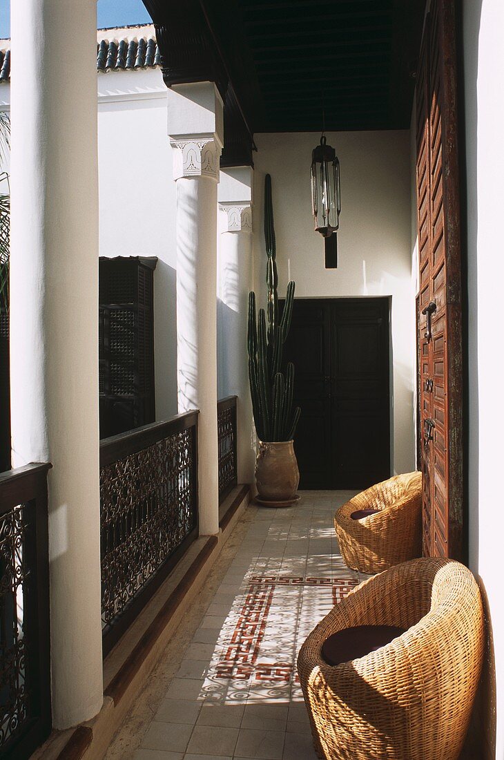 Balkon eines marokkanischen Hauses mit Säulen, Fliesenboden, Korbsesseln & Kaktus