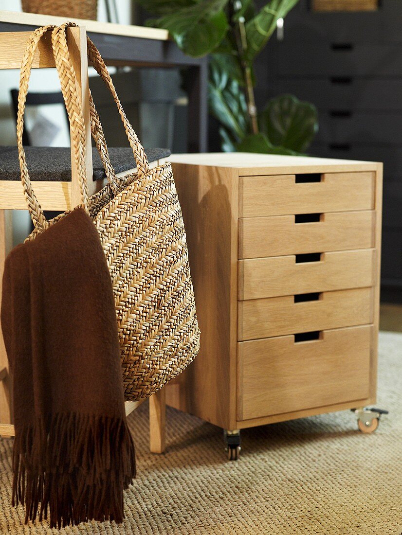 Rolling file cabinet out of wood with drawers and shopping basket hanging on a chair