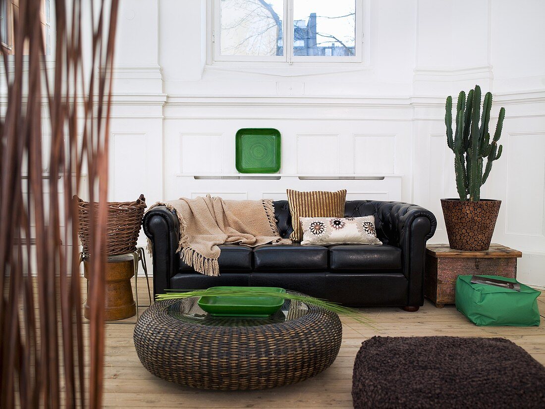 Rattan floor table in front of a black leather couch and cactus pot in a living room