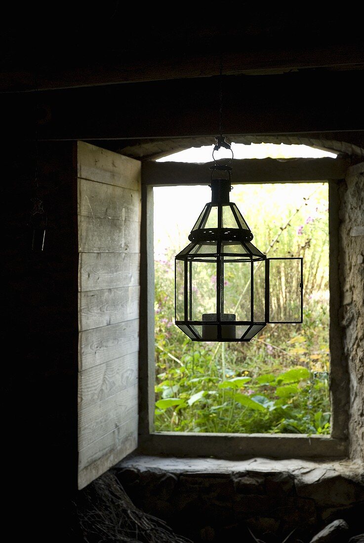 Laterne im offenen Fenster am Sturz hängend mit innenseitiger Holzlade und Blick auf Garten