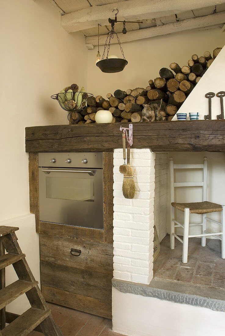 Küchenecke mit eingebautem Edelstahlofen im rustikalen Holzschrank neben Kamin und Kaminholzlager