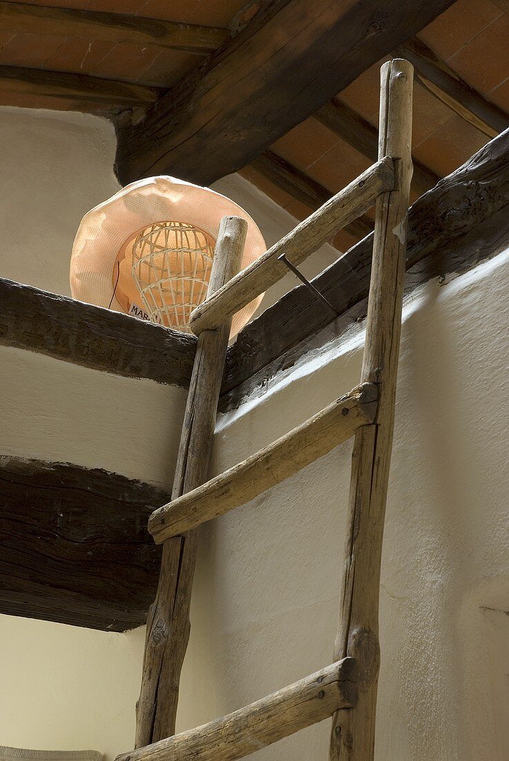 Wooden ladder leaning against a wall and attic floor with lamp and a hat as a lamp shade