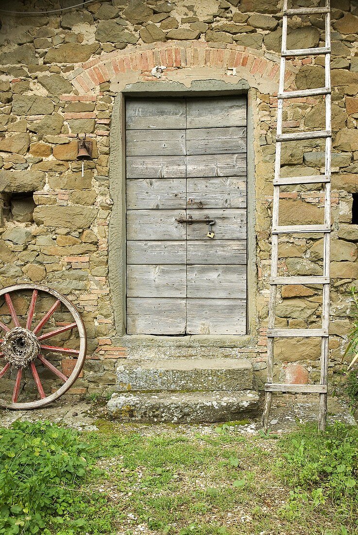 Ladder and wooden wheel in front of a natural stone facade with a wooden door