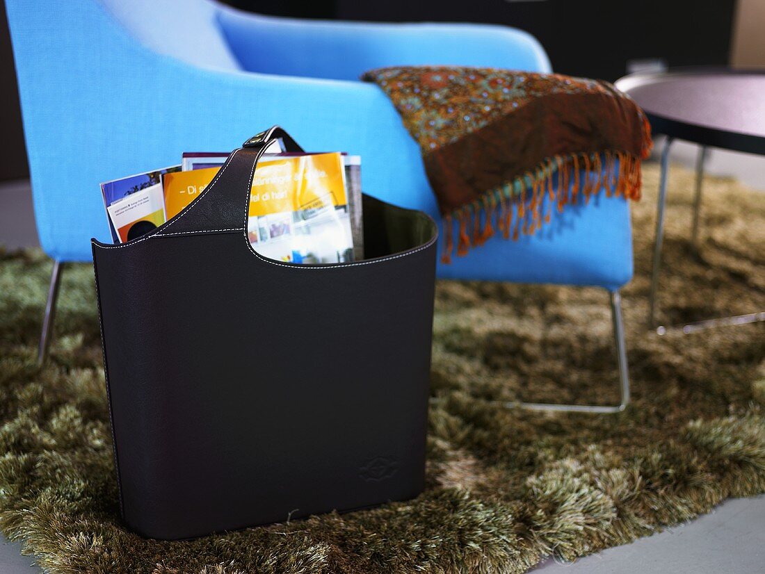 Schwarze Tasche mit Zeitschriften vor blauem Sessel