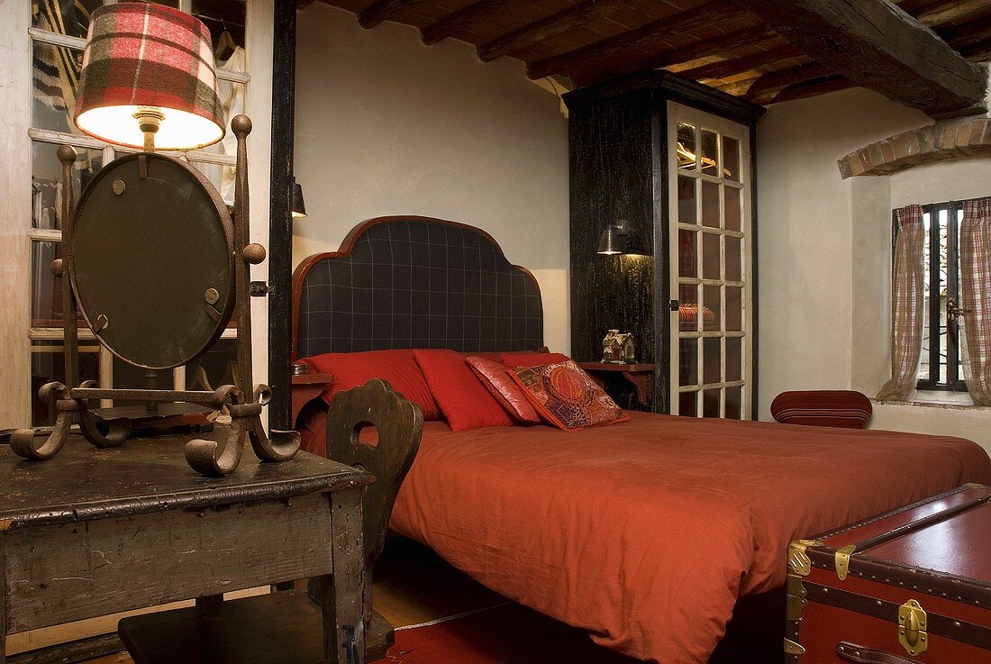 Bett mit gepolstertem Kopfteil und roter Bettwäsche im ländlichen Schlafraum