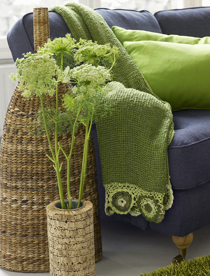 Pflanze im Topf mit Korkverkleidung vor einer Rattanvase und grüner Tagesdecke auf Sofa