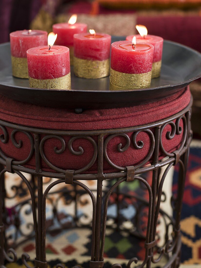 Burning, red candles with gold stripes on a black tray and upholstered stool