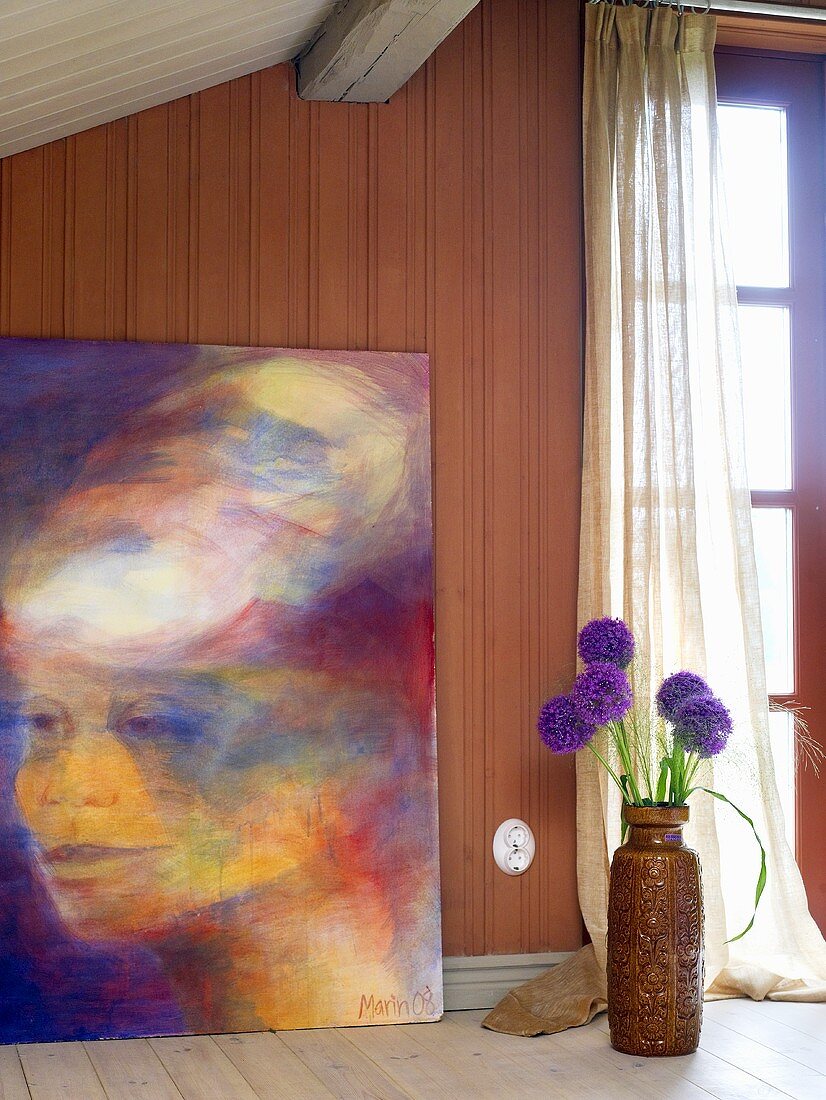 Picture leaning on a brown wood paneled wall and floor vase with flowers in front of a French door