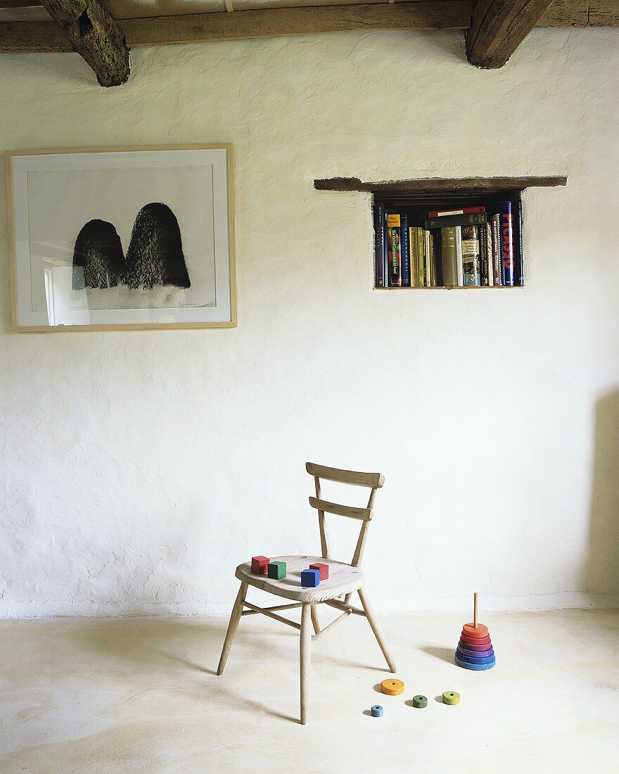 Schlichter Wohnraum mit Wurfspiel & bunten Holzwürfeln auf Holzstuhl, Wandnische als Bücherregal und Wandbild