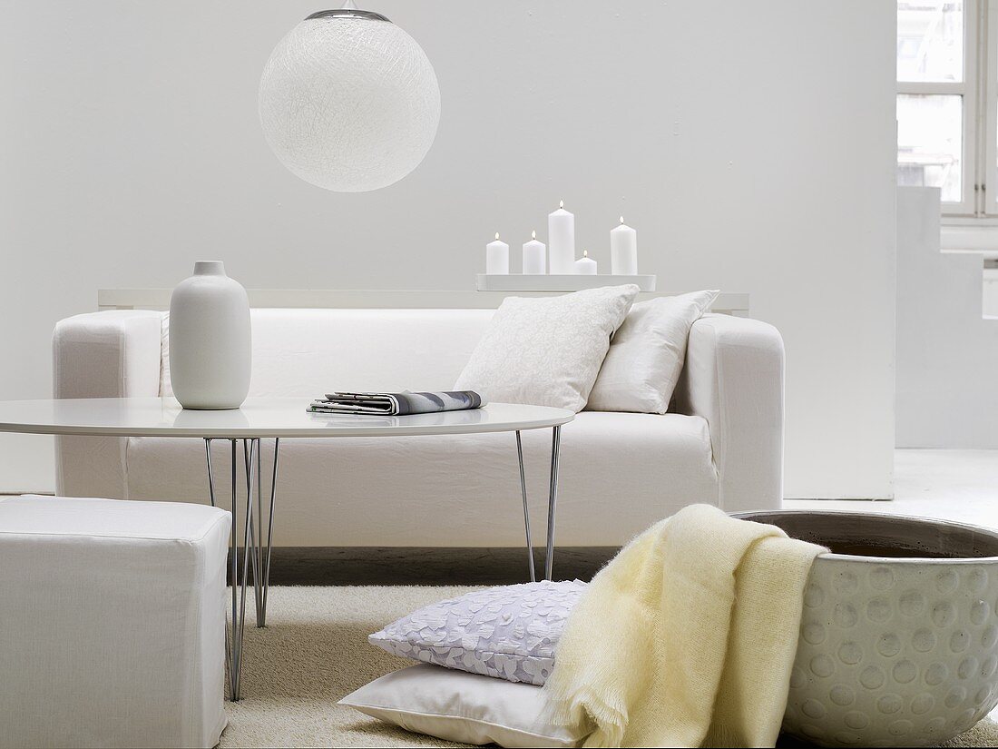 Coffee table with chrome legs in front of a white sofa and container with throw blanket